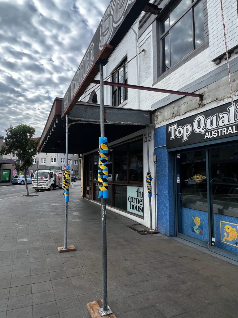Temporary support poles with hazard tape propping up an awning frame during repair work