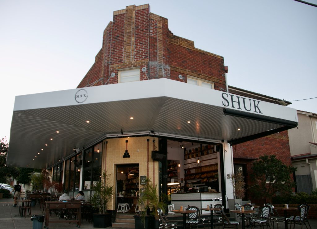 Corner shop front awning at Shuk restaurant in North Bondi with fascia lettering and a lit soffit