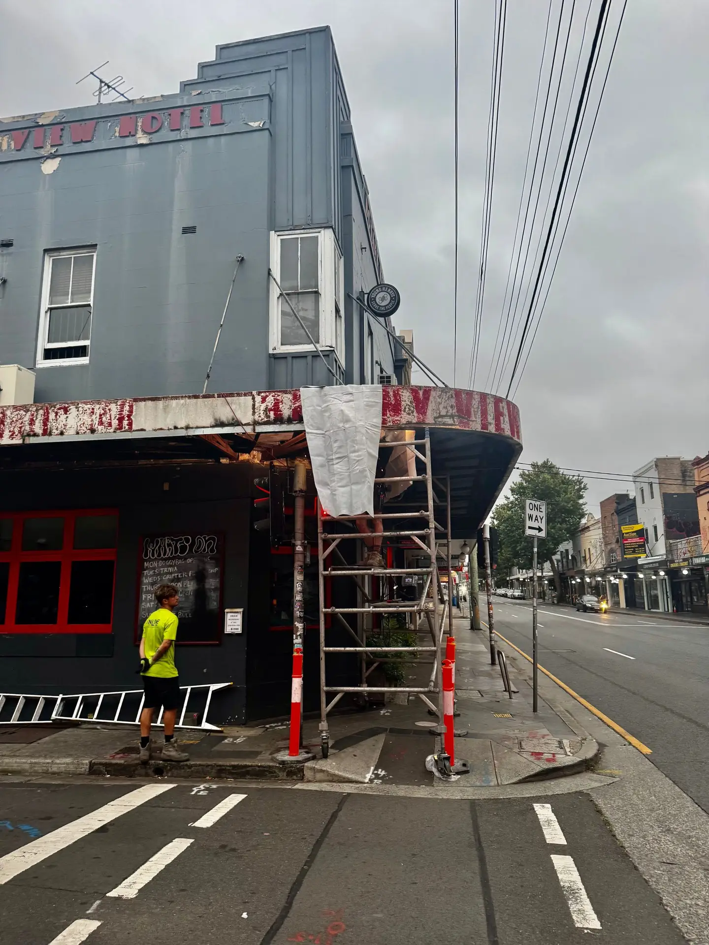 Tradesperson on scaffolding repairing the curved corner awning at a hotel shopfront in Sydney
