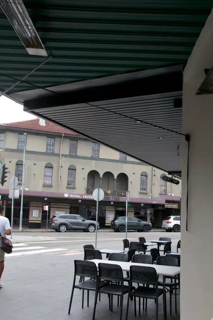 Newly installed angled slatted metal awning shading an outdoor dining area, overlooking the Royal Hotel in Bondi
