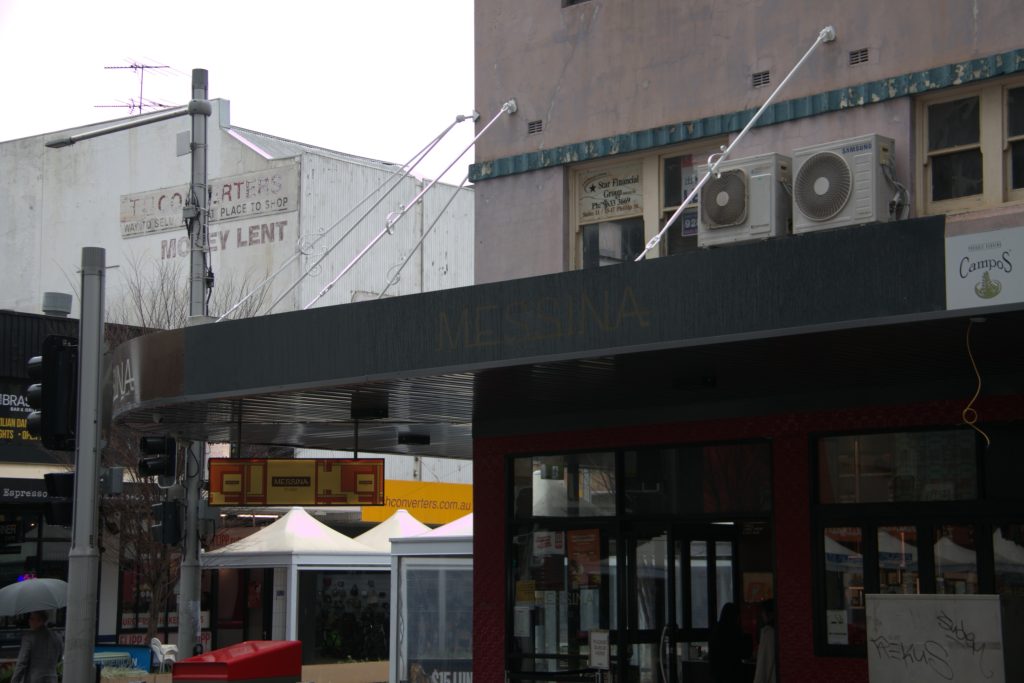 Wrap-around corner awning with tie-rod supports at the Messina shopfront
