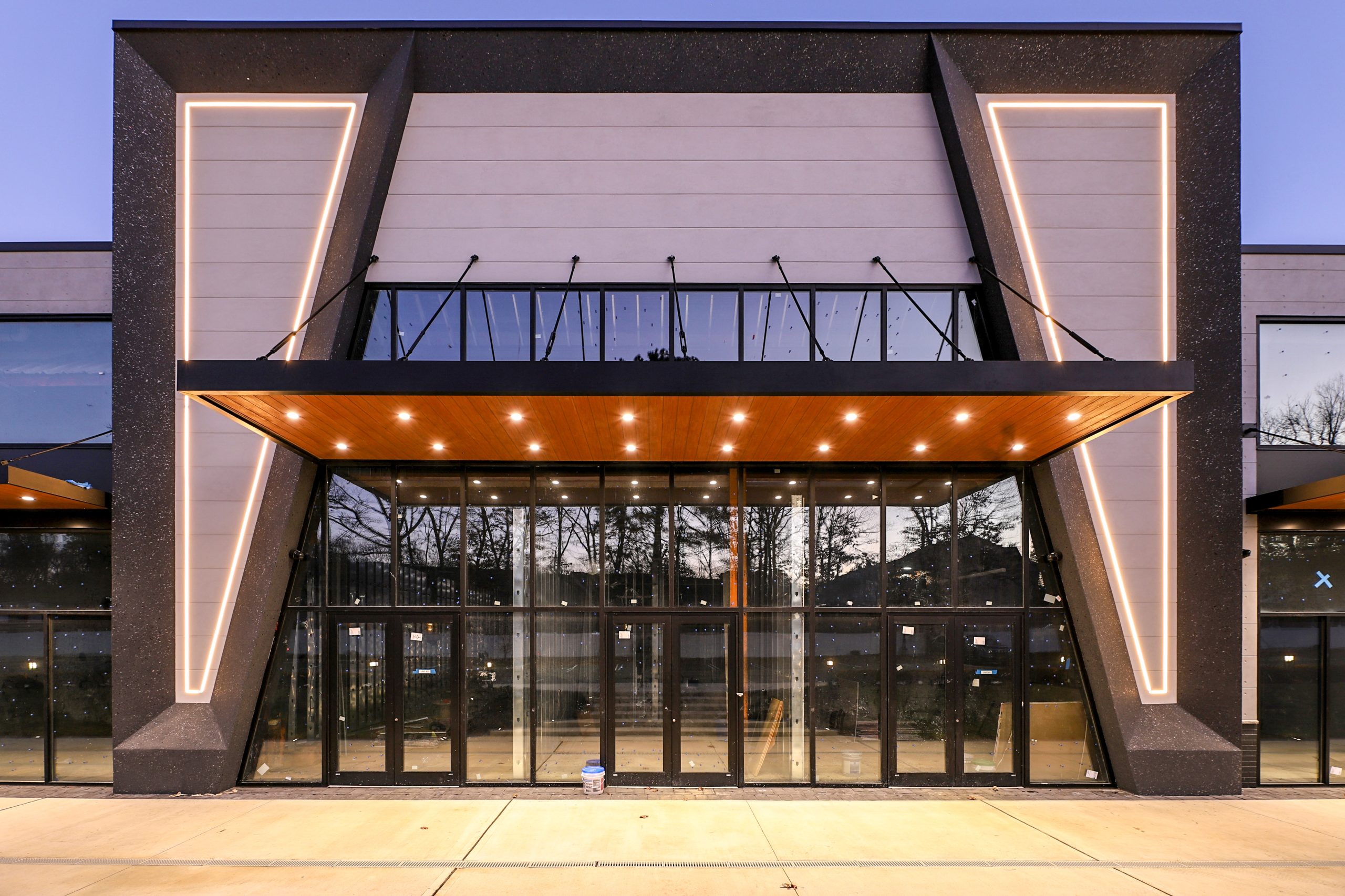 Modern commercial building entrance with a suspended timber-lined awning and tie-rod supports