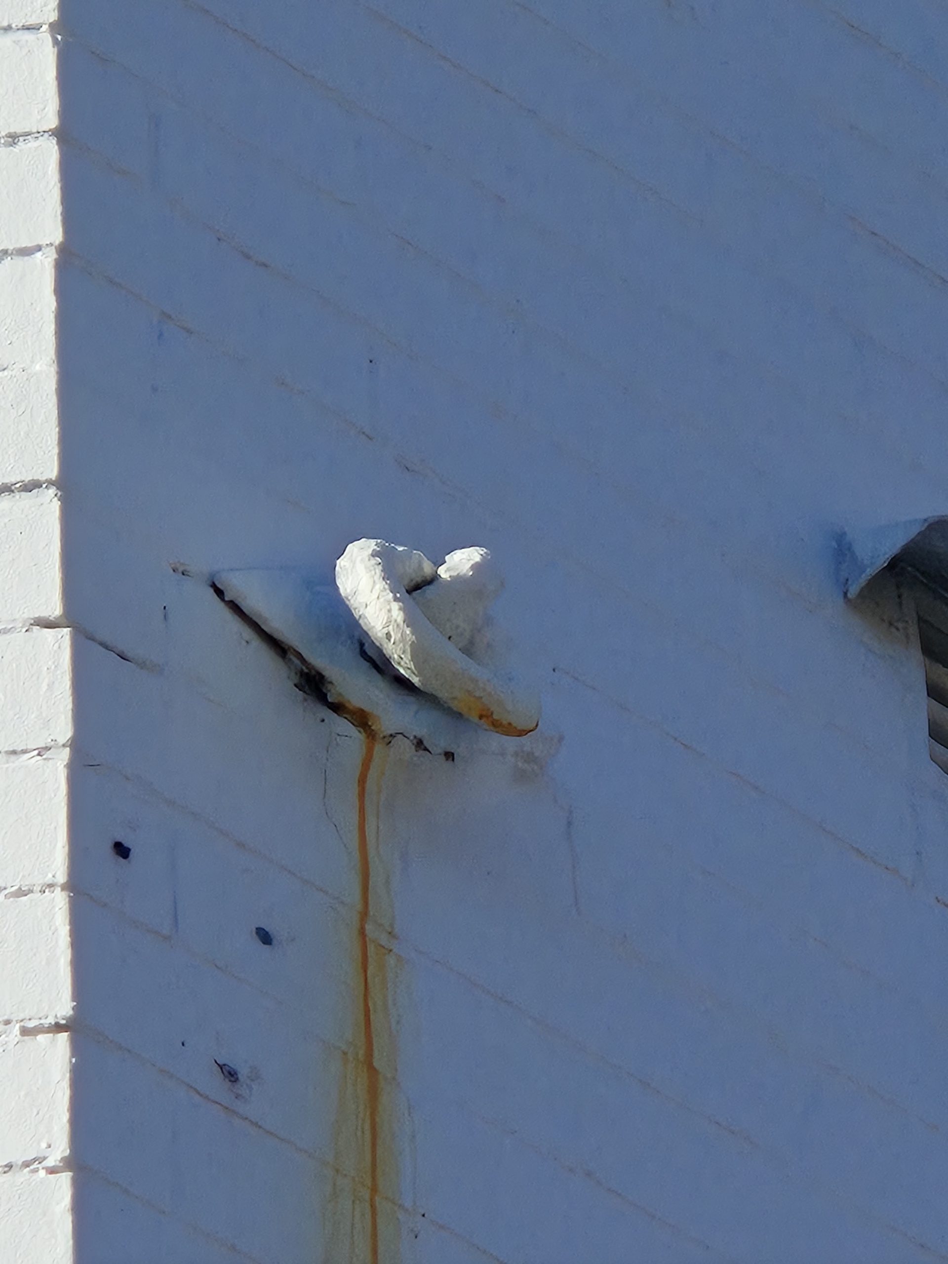 Rusted anchor plate bolted to a brick wall with a rust stain, a damaged tie-rod anchor point