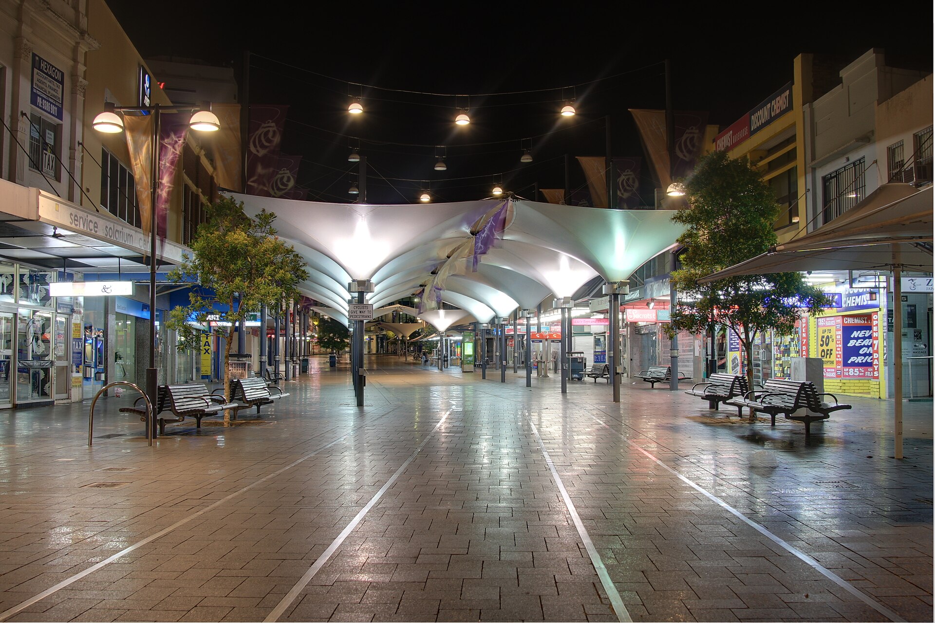 Oxford Street pedestrian mall with shade canopies over shopfronts at night, Bondi Junction