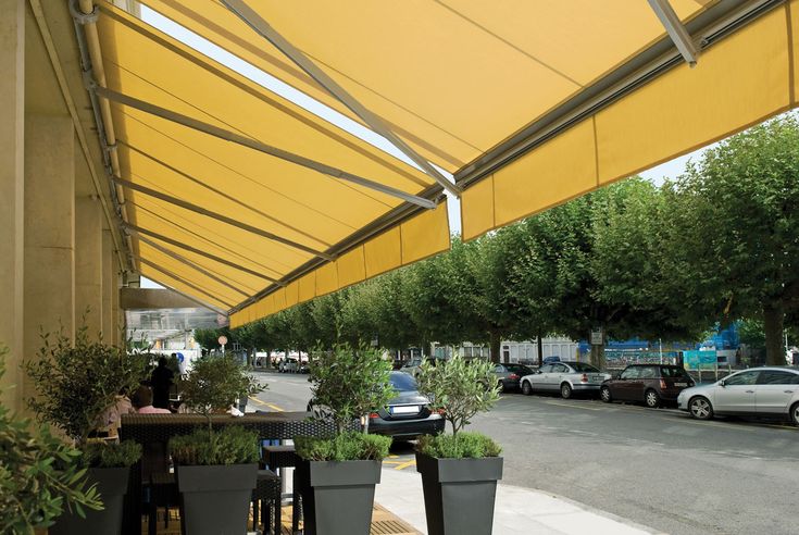 Large yellow retractable folding-arm awning extended over an outdoor dining terrace