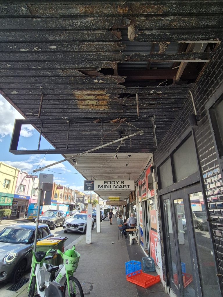 Rotting black soffit linings falling away under a street awning on Bondi Road