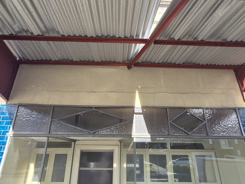 Corrugated steel awning roof with rusted steel support beams and a cracked rendered fascia above a Sydney shopfront