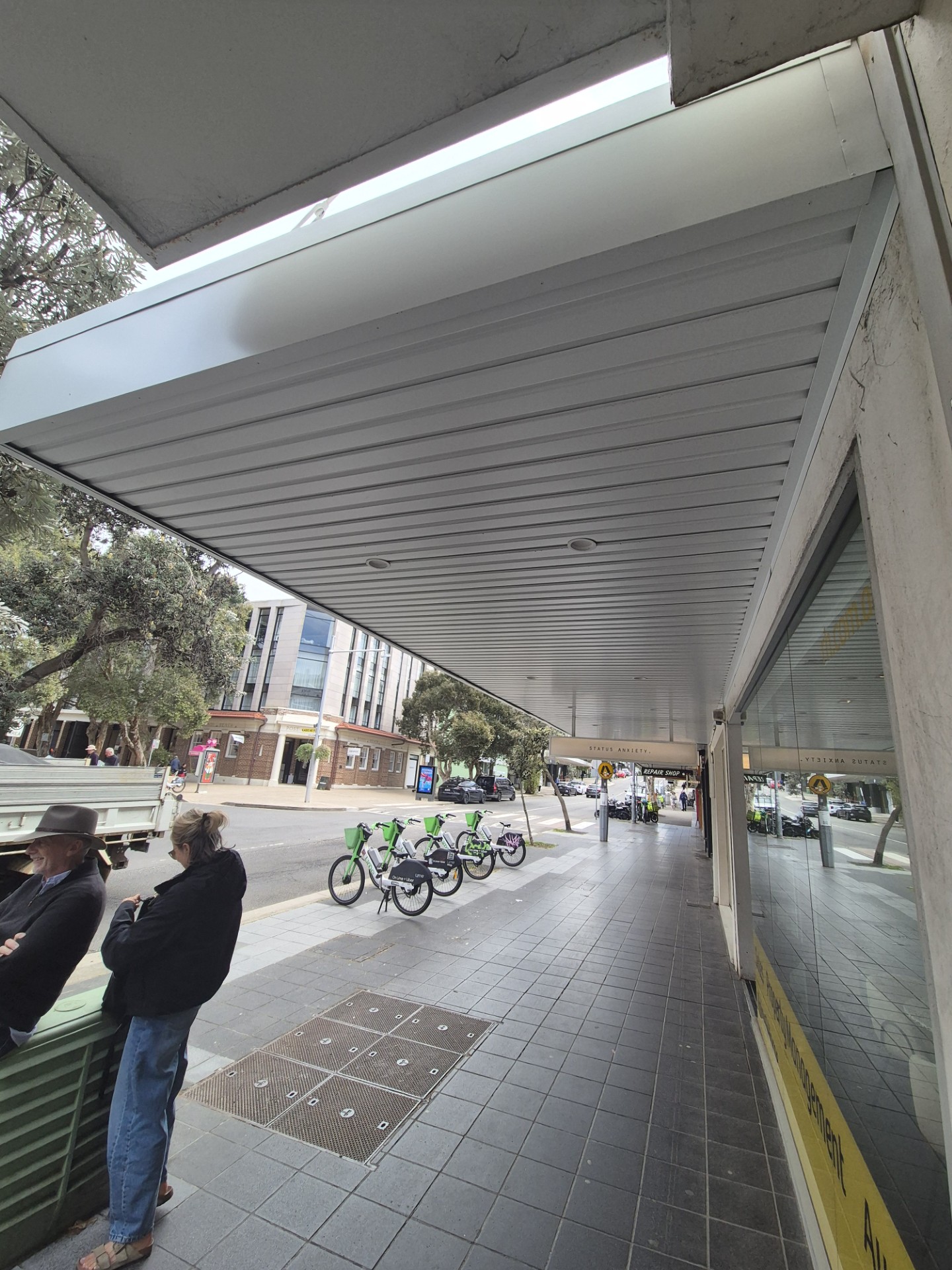 Underside of a repaired street awning on Hall Street, Bondi Beach, with people walking on the footpath below